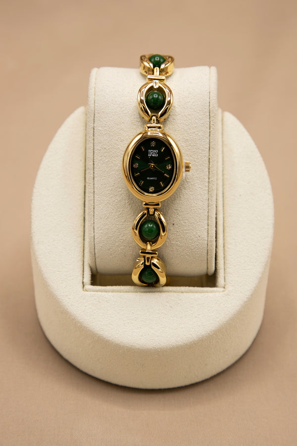 feminine vintage looking gold watch with black face and deep green stone weaved bracelet band